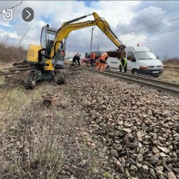RoxKop - Prace Ziemne Sebastian Górecki - Żółta mini koparka na torach kolejowych wysypuje żwir, grupa robotników w odblaskowych ubraniach pracuje obok białego vana.