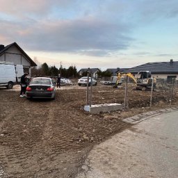 RoxKop - Prace Ziemne Sebastian Górecki - Żółta mini koparka na placu budowy z widocznymi fundamentami, samochodem osobowym i dostawczym w tle, pod pochmurnym niebem.