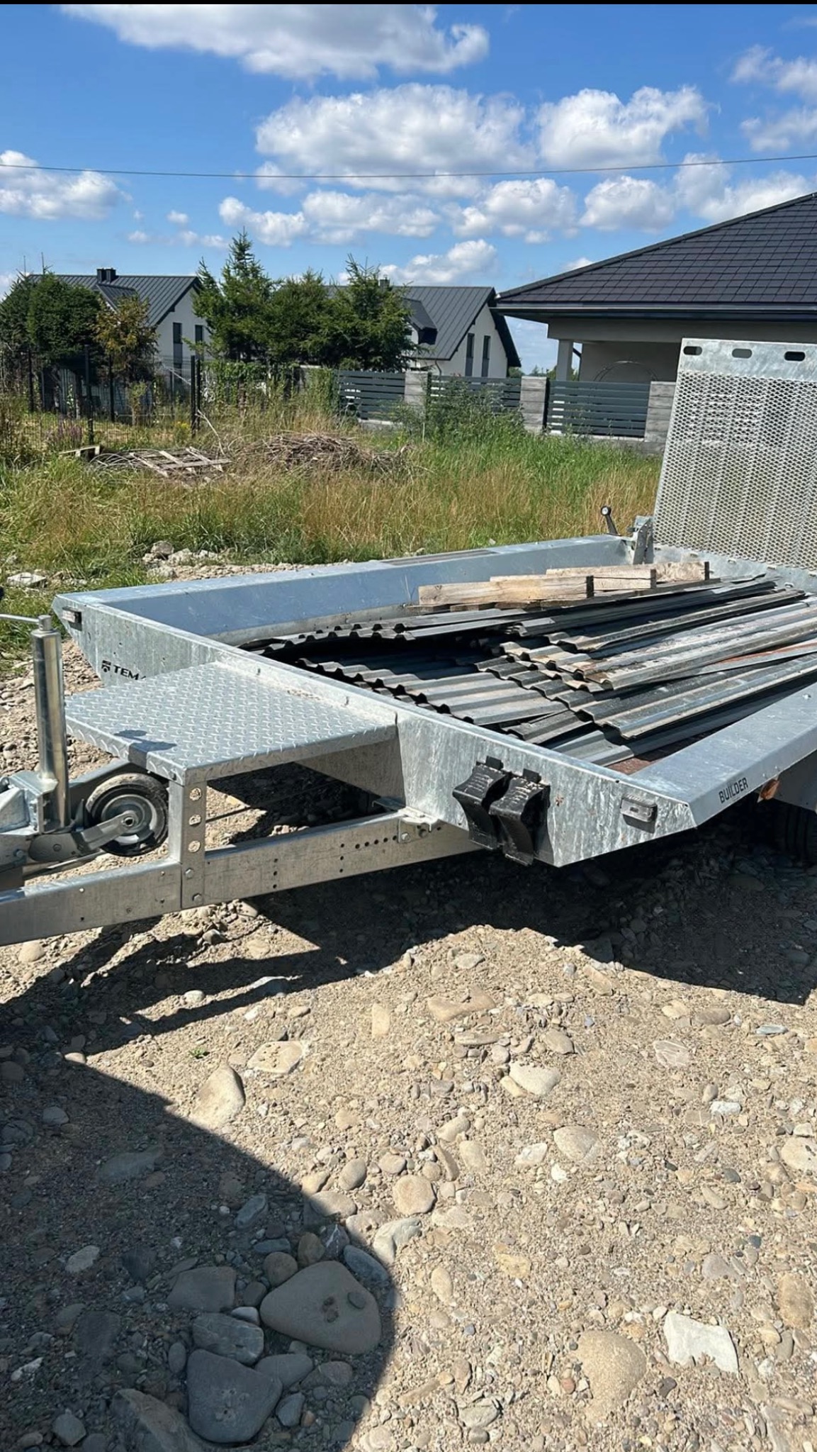 Laweta z metalowymi elementami konstrukcyjnymi na tle domów jednorodzinnych i błękitnego nieba.