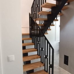 Metalovo - Nowoczesne schody metalowe z drewnianymi stopniami i czarną, geometryczną balustradą. Widok z dołu, marmurowa podłoga, minimalistyczny design.