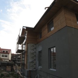 BigRem Plus - Budynek w trakcie ocieplania i wykańczania elewacji, widoczne rusztowania, ocieplenie styropianem, fragmenty elewacji pokryte drewnem, dolna część elewacji w szarym tynku