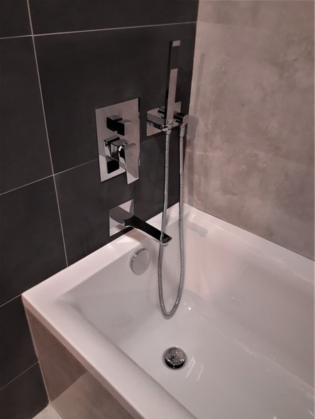 Biała wanna z nowoczesną chromowaną armaturą w łazience wykończonej ciemnoszarą i jasnoszarą płytką.