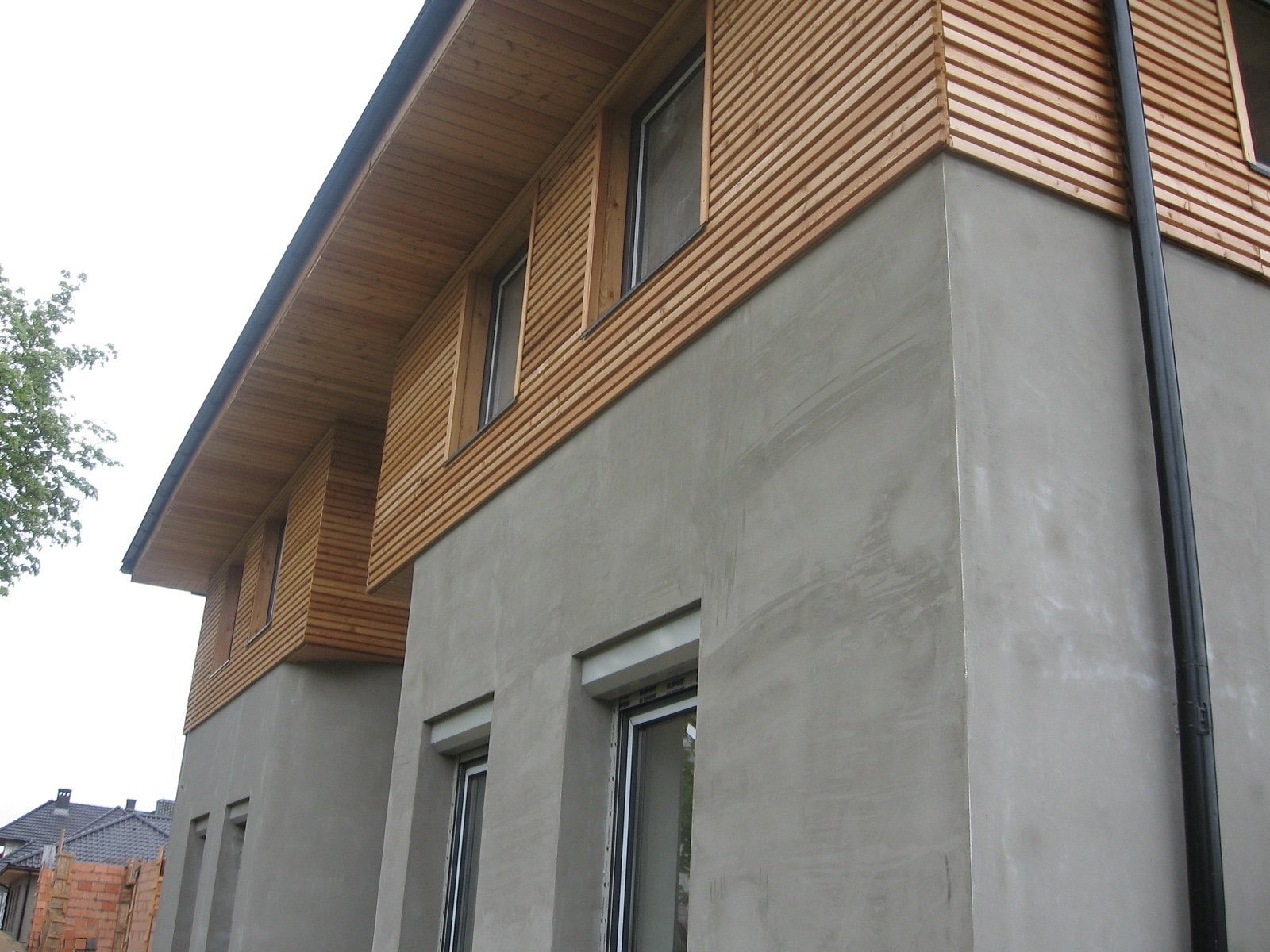 Elewacja budynku w Gdańsku z surową, szarą fakturą i drewnianą okładziną z poziomych listew, widoczny fragment rynny.