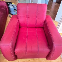 Pucuś pranie tapicerki i dywanów Patryk Zdrzalik - Czerwony fotel tapicerowany z widocznymi śladami użytkowania, obok odkurzacz piorący i fragment drugiego fotela, na drewnianej podłodze.