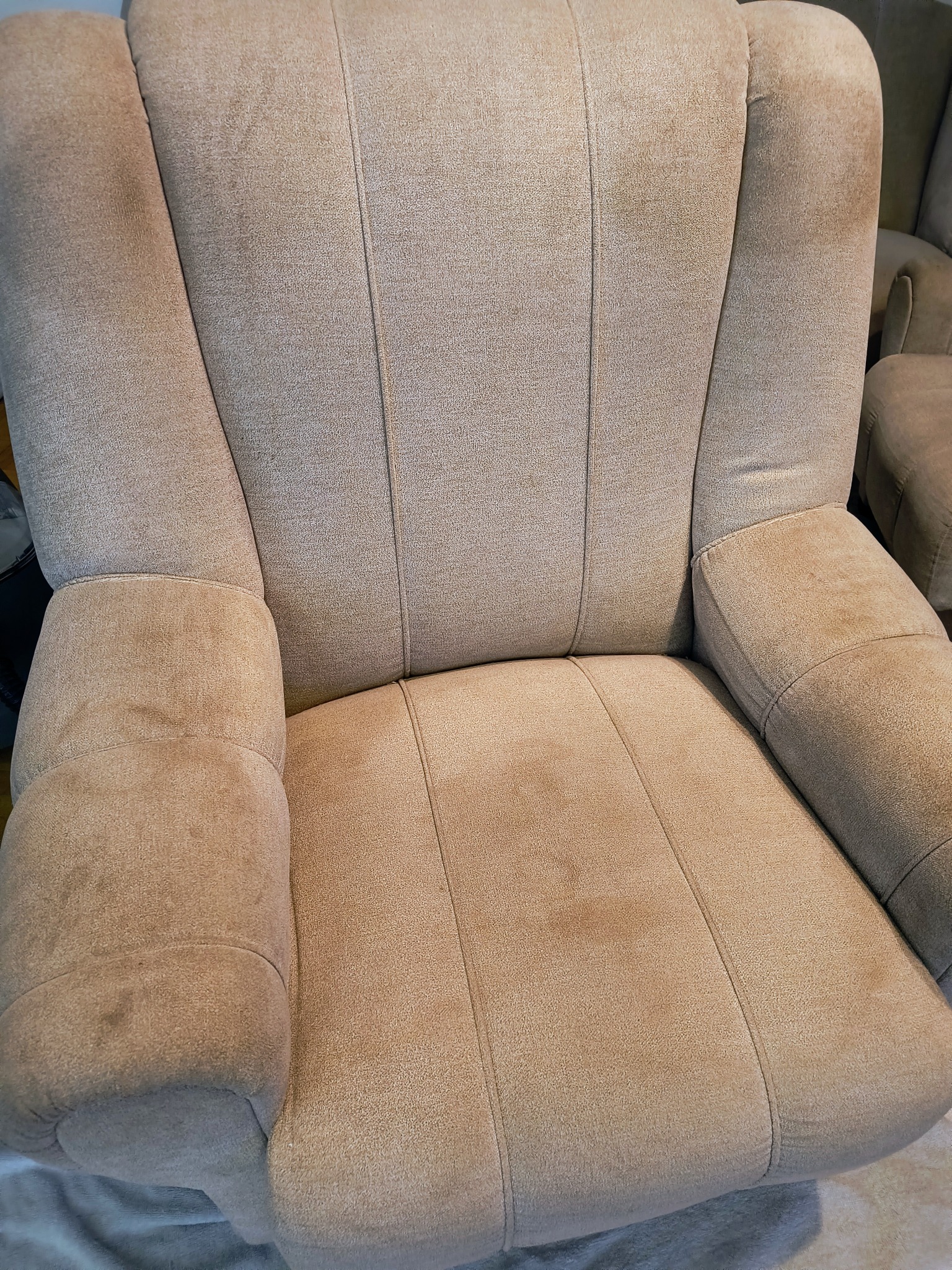 Beżowy fotel tapicerowany z widocznymi plamami na siedzisku i podłokietnikach, ukazujący potrzebę odświeżenia.