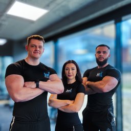 Lifepeak Trainers - Zespół trzech trenerów personalnych w czarnych strojach sportowych z logo, pozujących na tle siłowni z dużym oknem i betonowym sufitem.
