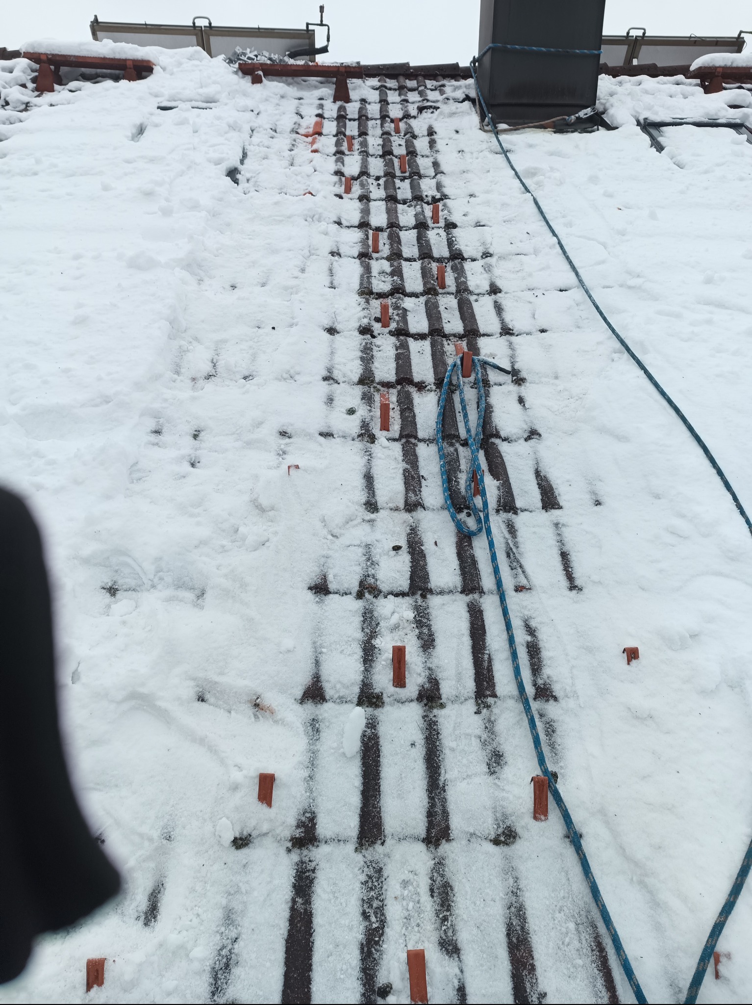 Śnieg na dachu z zamontowanymi uchwytami i liną asekuracyjną, widok z góry.