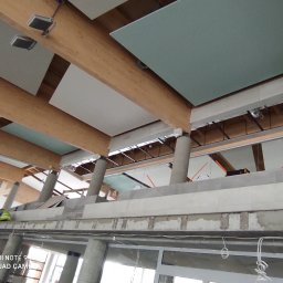 WK CONSTRUCTION SPÓŁKA Z OGRANICZONĄ ODPOWIEDZIALNOŚCIĄ - Montaż sufitu podwieszanego z płyt kartonowo-gipsowych na drewnianej konstrukcji nośnej, widoczni pracownicy w kamizelkach odblaskowych na rusztowaniu.