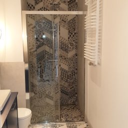 WK CONSTRUCTION SPÓŁKA Z OGRANICZONĄ ODPOWIEDZIALNOŚCIĄ - Nowoczesna łazienka z kabiną prysznicową wykończoną wzorzystymi płytkami, kontrastującymi z jasną podłogą ułożoną w jodełkę i białym grzejnikiem drabinkowym.