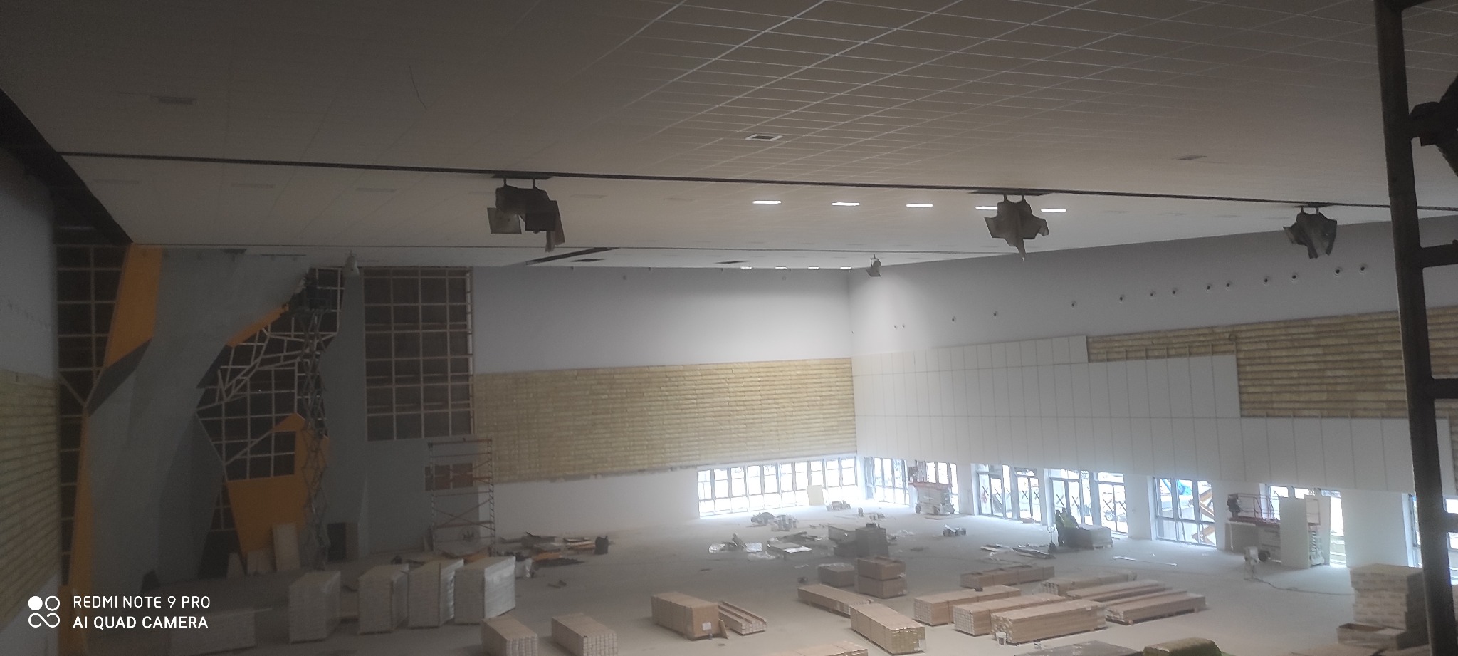 Przestronne wnętrze hali w trakcie wykańczania, widoczne konstrukcje ścian z płyty karton gips, metalowe rusztowania i materiały budowlane na podłodze.