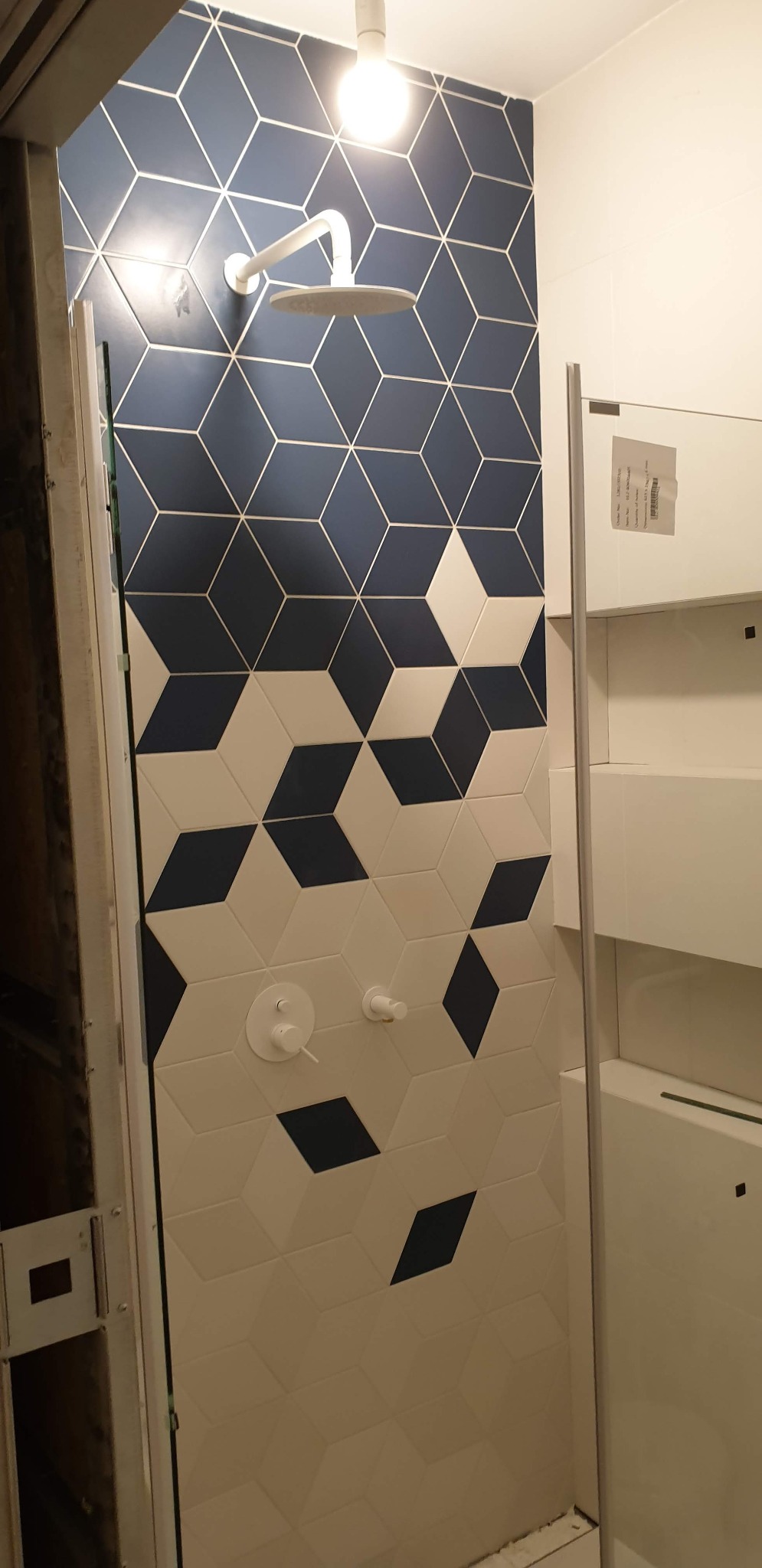 Nowoczesna kabina prysznicowa z geometrycznym wzorem z płytek w odcieniach bieli i granatu, minimalistyczna armatura, widoczne elementy konstrukcyjne kabiny.