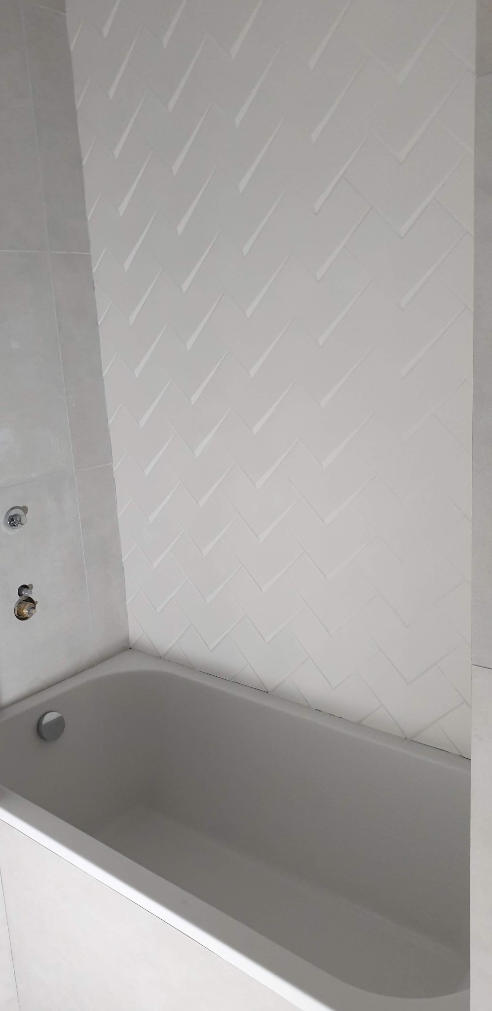 Biała wanna z widoczną ścianą wyłożoną płytkami w jodełkę, armatura w trakcie montażu.