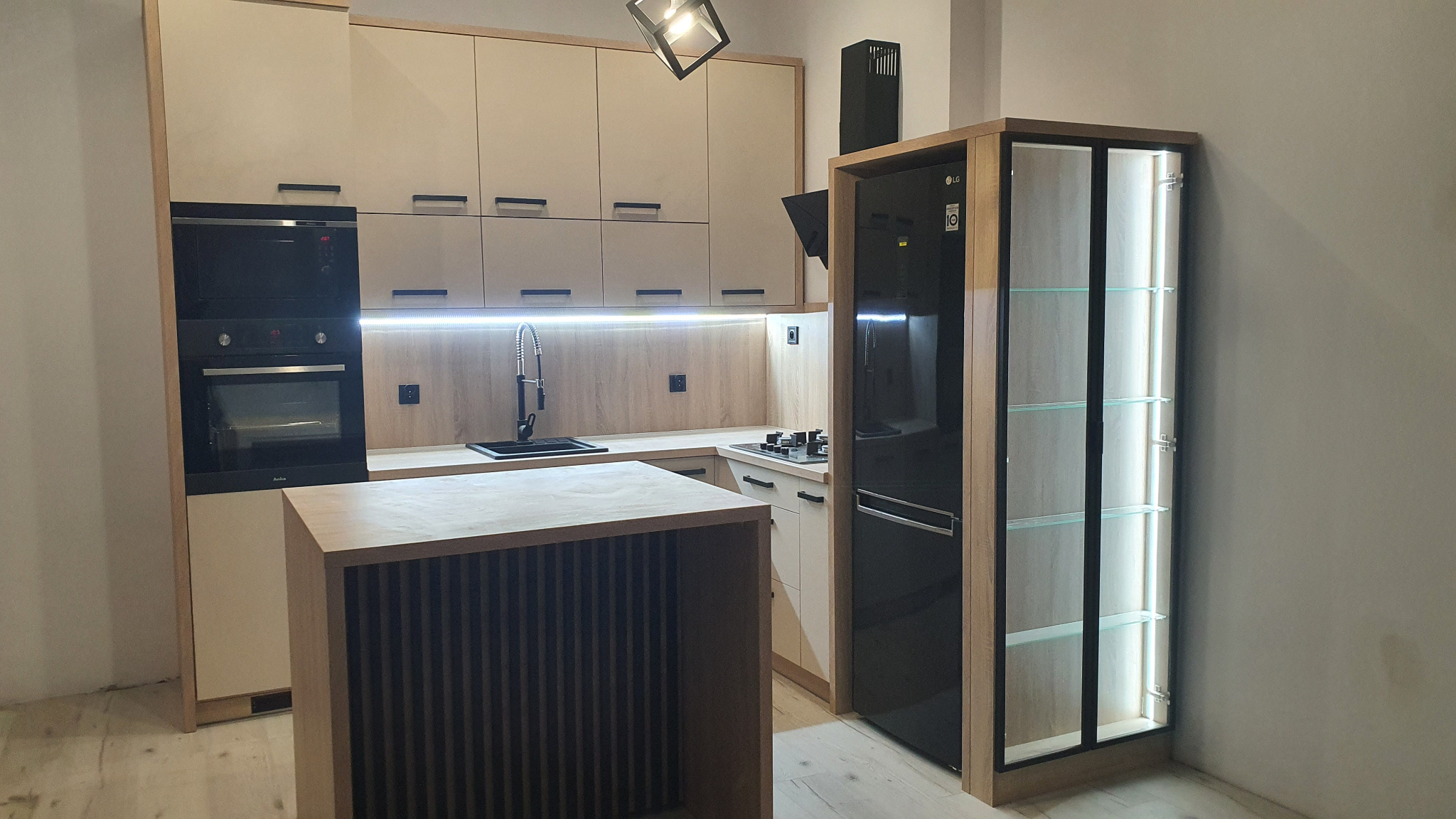 Nowoczesna kuchnia z jasnymi frontami, czarnym sprzętem AGD i wyspą z lamelami, oświetleniem LED pod szafkami i przeszkloną witryną z podświetleniem.