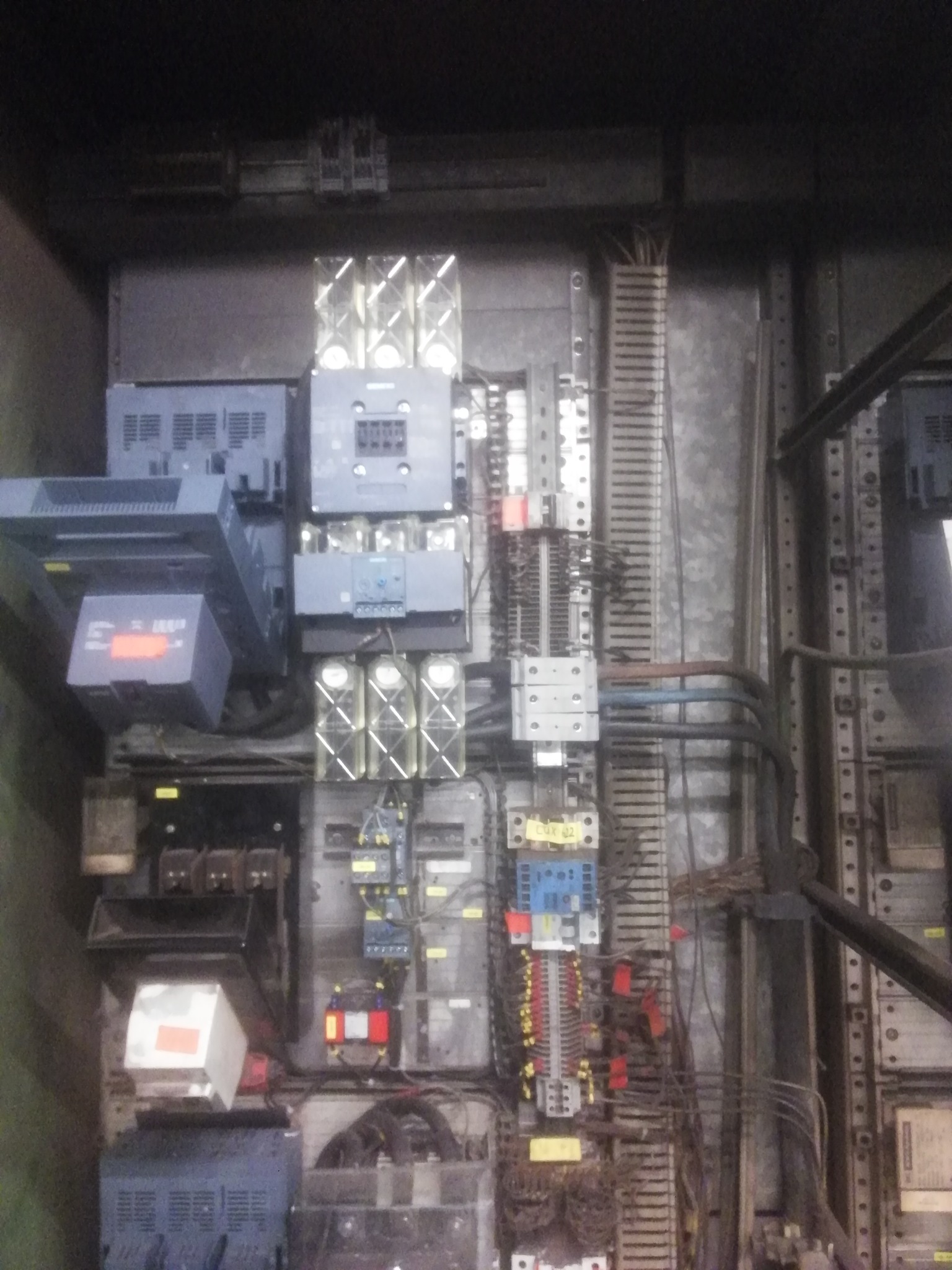 Rozbudowana szafa sterownicza z licznymi modułami, bezpiecznikami i okablowaniem, widoczne elementy marki Siemens. Szafa w szarej obudowie z metalowymi szynami DIN i listwami zaciskowymi.