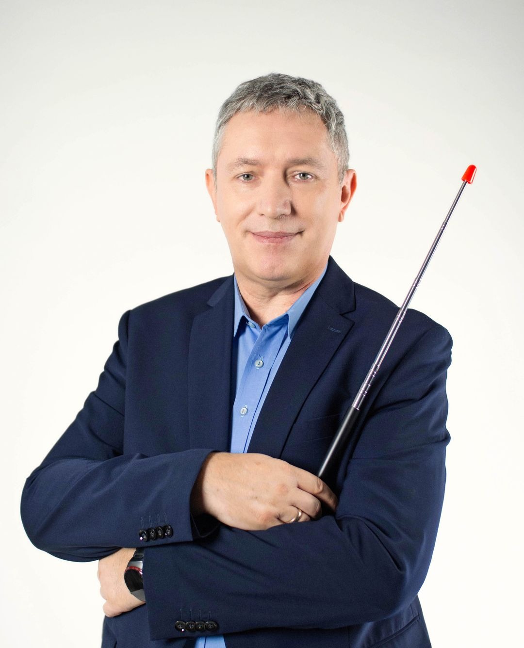 Portret uśmiechniętego mężczyzny w garniturze, trzymającego teleskopową antenę z czerwoną końcówką na jasnym tle.