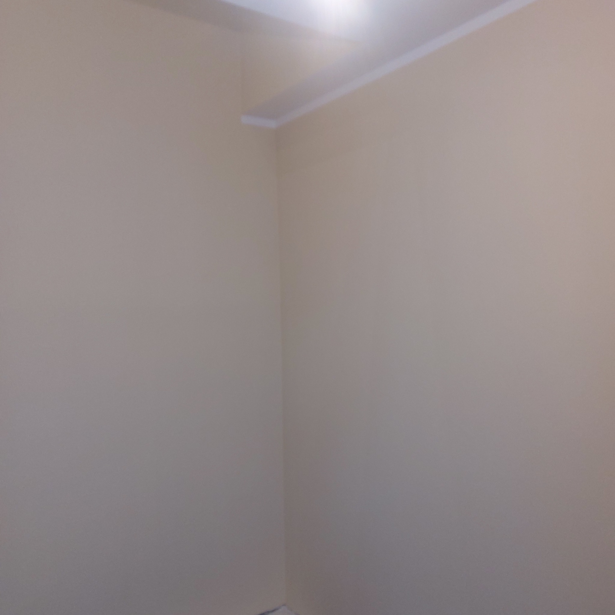 Pomalowany na beżowo narożnik pokoju z białą listwą przysufitową, widok z dołu.