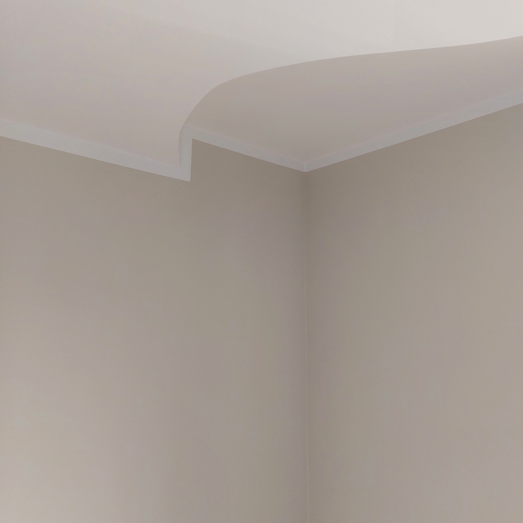 Wnętrze z beżowymi ścianami, białym sufitem i ozdobnym, białym wykończeniem na styku ściany i sufitu, widok na róg pomieszczenia.