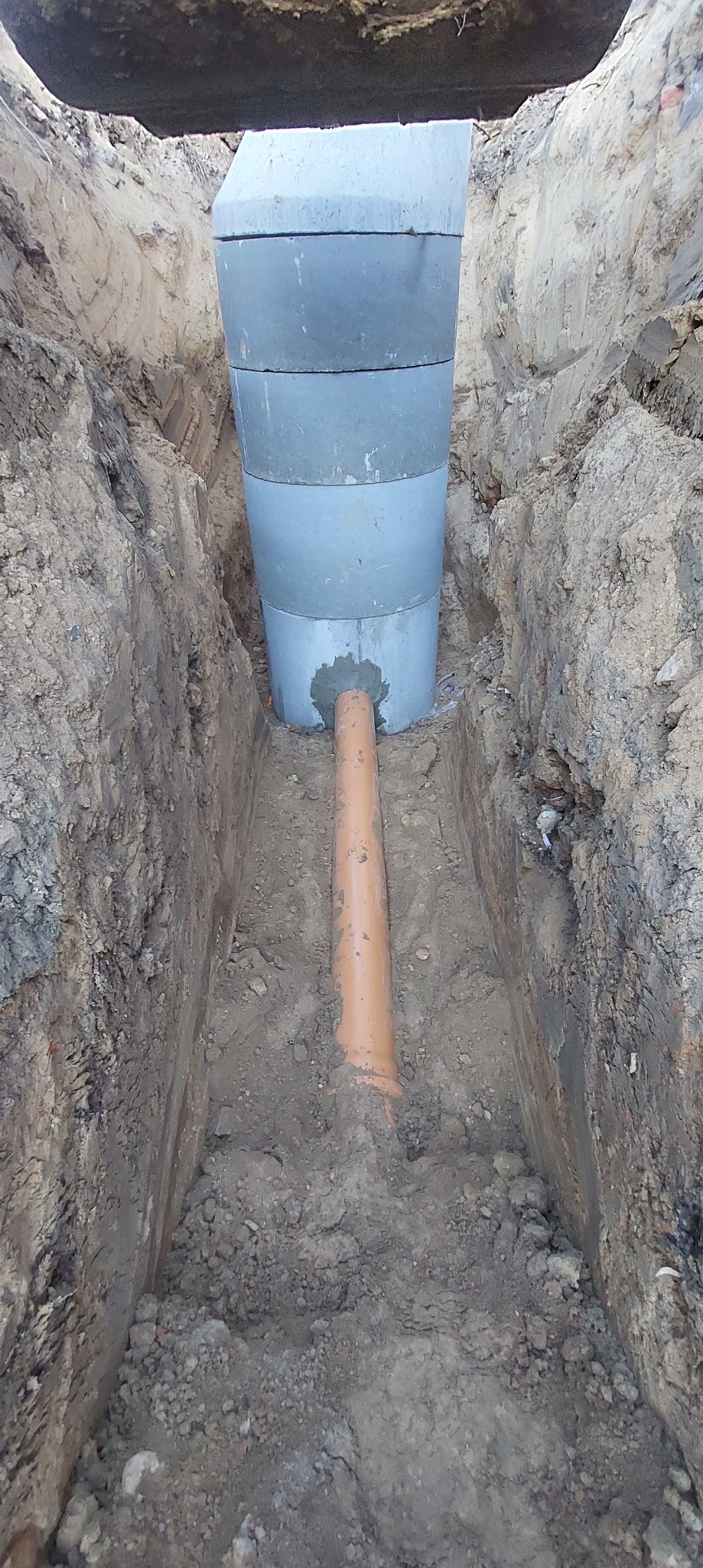 Wykop z betonowym zbiornikiem segmentowym i wpiętą rurą kanalizacyjną.