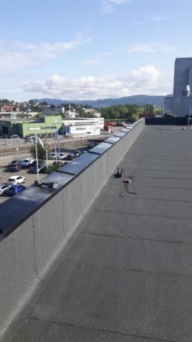 Płaski dach pokryty papą termozgrzewalną, widok na miasto i góry w tle, z widocznymi elementami wentylacji i zabezpieczeń krawędzi.