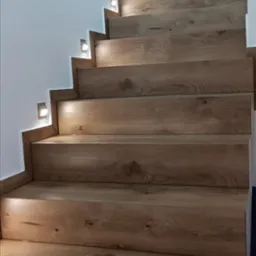 Drewnopodobne schody z podświetleniem LED w ścianie, widok z dołu.