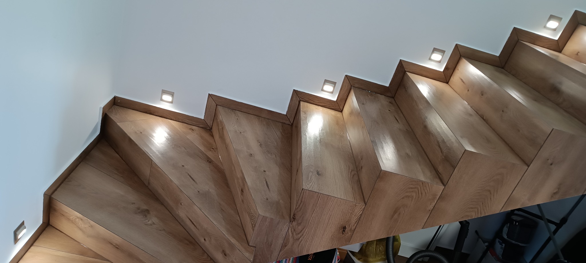 Nowoczesne schody drewniane z oświetleniem punktowym w suficie, widok od dołu.