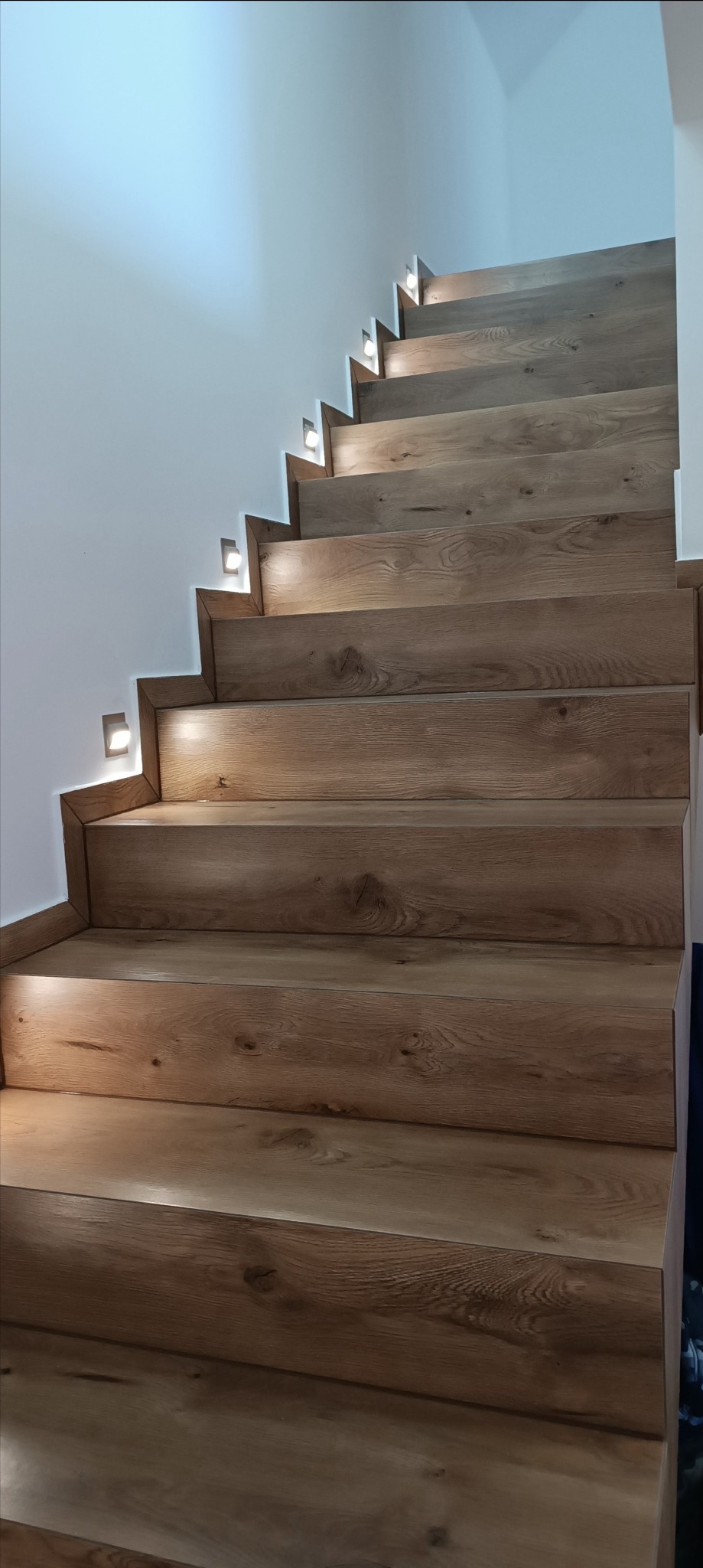 Drewnopodobne schody z podświetleniem LED w ścianie, widok z dołu.