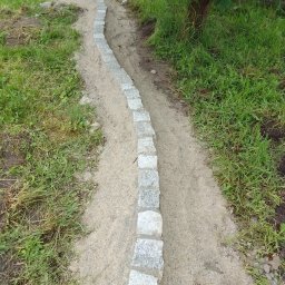 Toms-bruk - Krawężnik z kostki granitowej oddzielający trawnik od ścieżki z piasku, widok z góry.