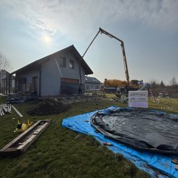 Profi Trax Rafał Jeglorz - Wylewka betonu do fundamentów domu jednorodzinnego przy użyciu pompy do betonu, widoczne szalunki, izolacja termiczna, przygotowany teren pod budowę.