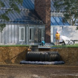 Profi Trax Rafał Jeglorz - Wykop z widoczną podziemną instalacją zbiornika na ścieki, z podłączeniem do domu i pracownikiem spłukującym teren wodą z węża.