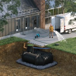 Profi Trax Rafał Jeglorz - Wizualizacja przekroju ziemi z zainstalowaną przydomową oczyszczalnią ścieków z tworzywa sztucznego, z podłączonymi rurami, na betonowej podsypce, z trawnikiem, podlewającym go mężczyzną z wężem...