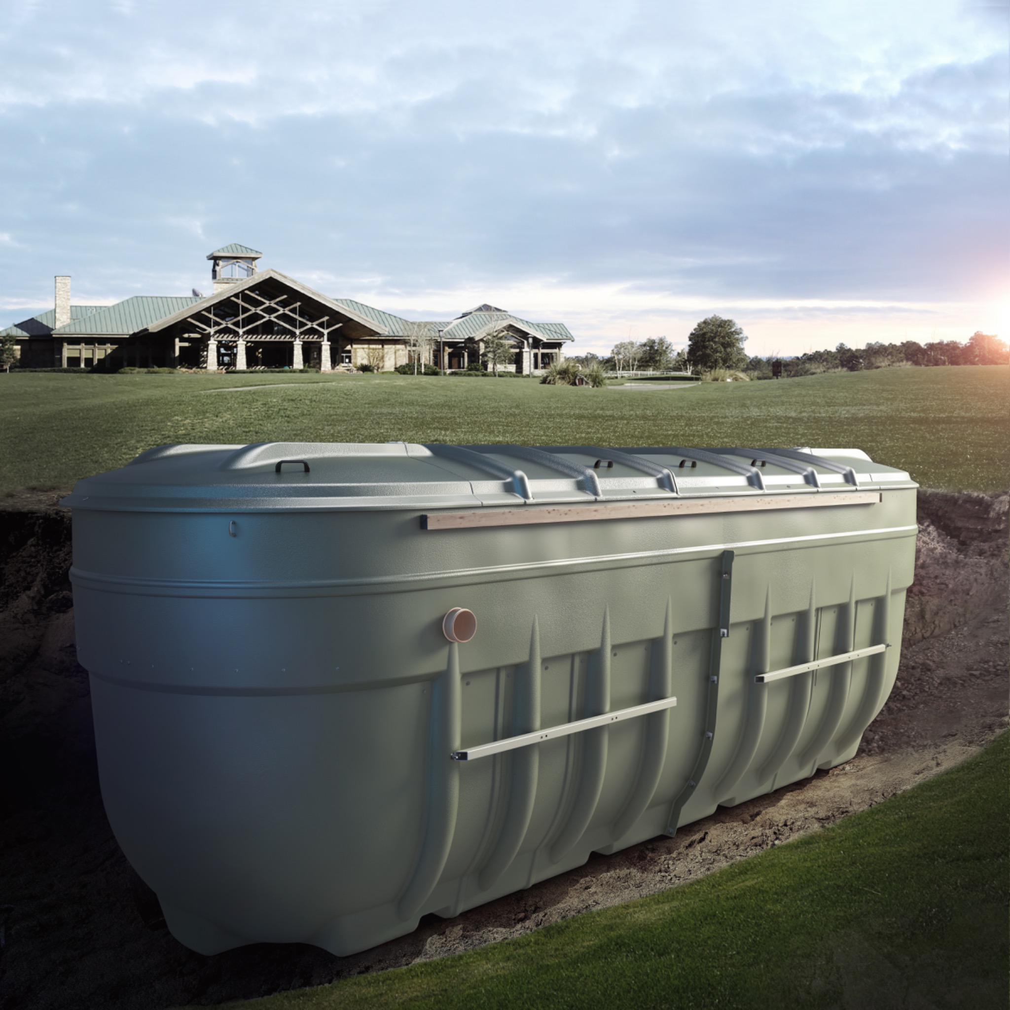 Zielony, plastikowy zbiornik zakopany w ziemi na tle budynku z zielonym dachem i rozległym trawnikiem, widoczne elementy montażowe i rura odpływowa.
