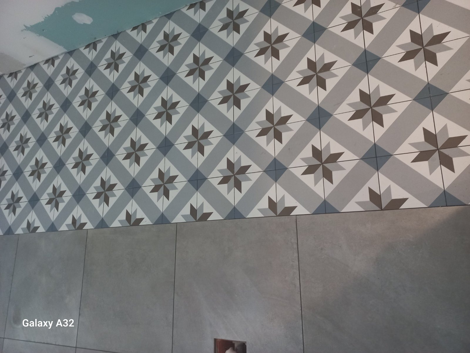 Ściana wykończona płytkami ceramicznymi w geometryczny wzór gwiazd, z szarą lamperią dolną, widoczny fragment sufitu w trakcie prac wykończeniowych.