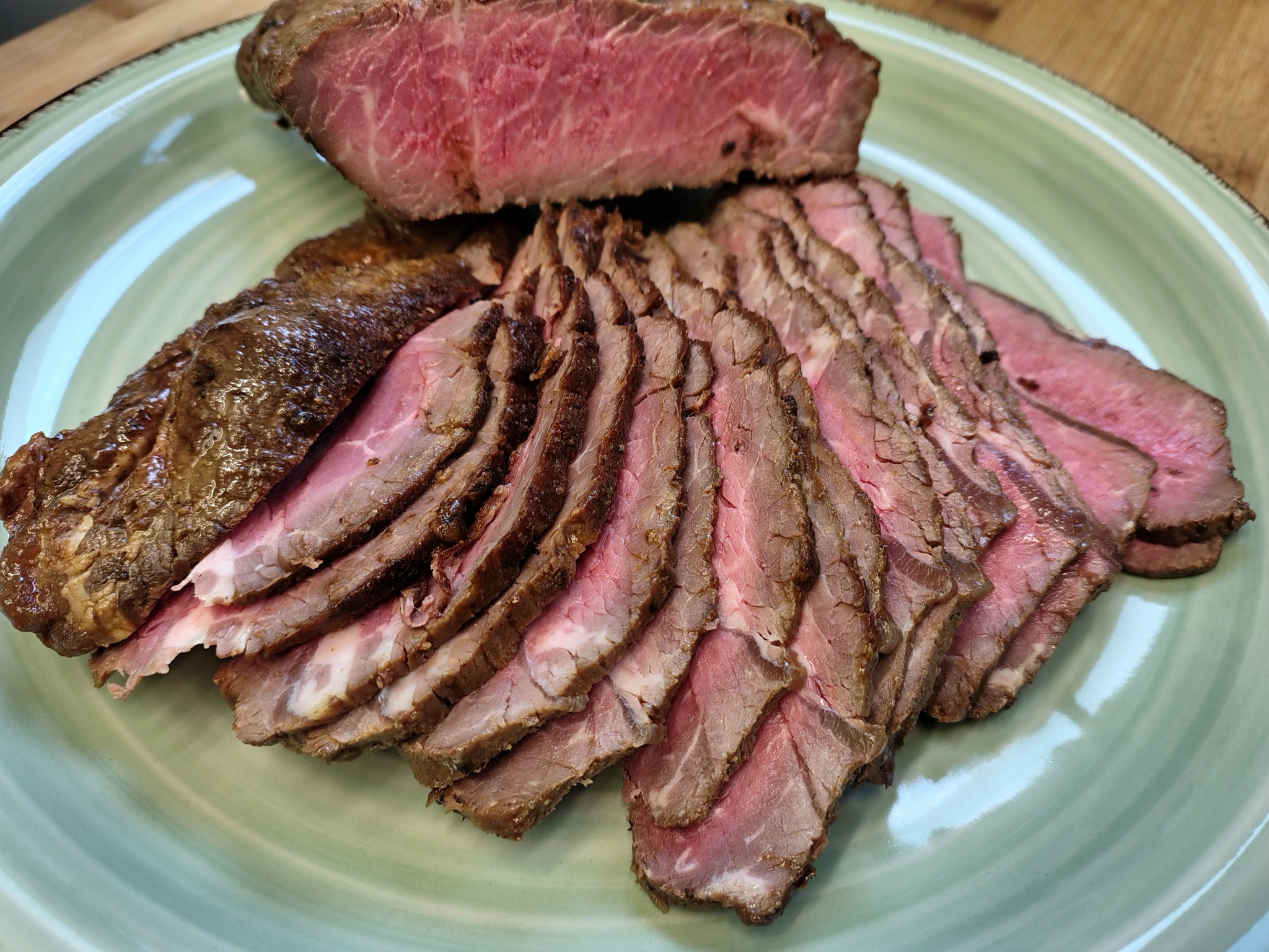 Krojony rostbef na zielonym talerzu, z wyraźnie widoczną strukturą mięsa i stopniem wysmażenia.