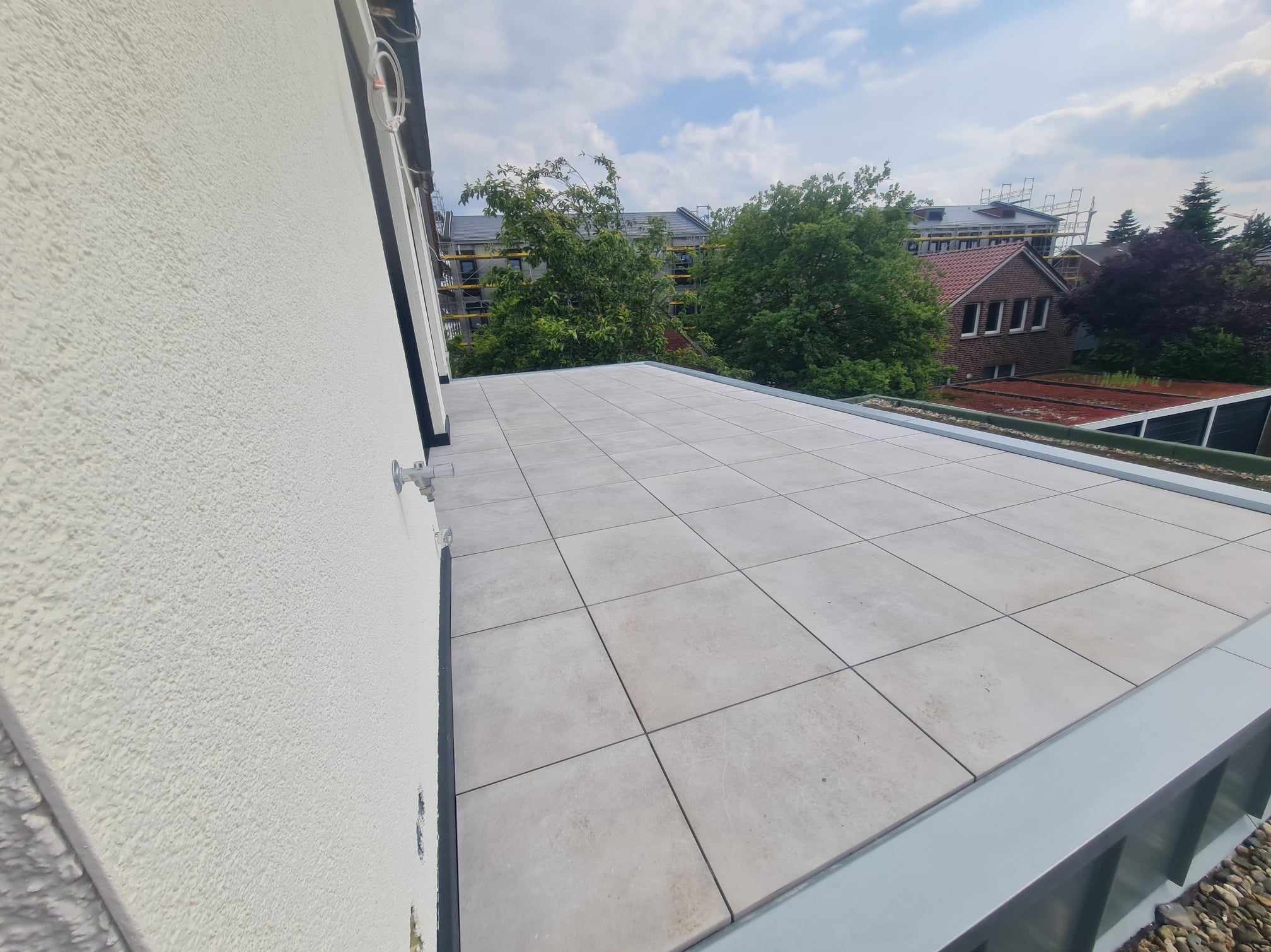 Wykończony płaski dach pokryty jasnoszarymi płytami ceramicznymi, widok z góry na tle zabudowy mieszkalnej i zieleni.