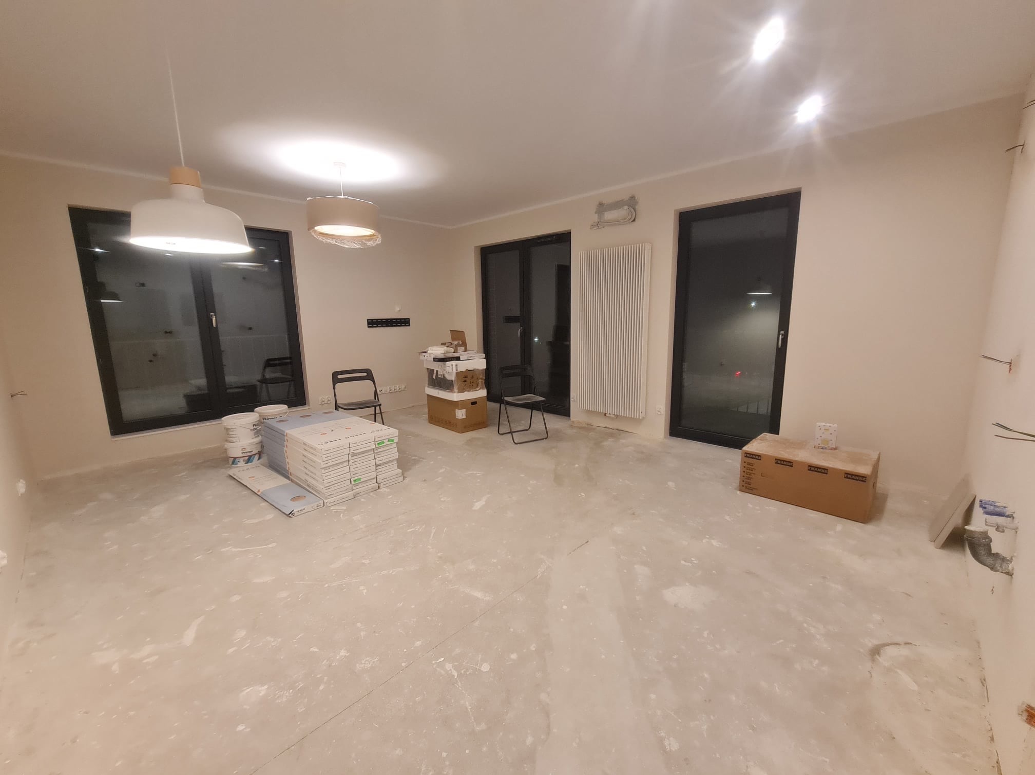 Wnętrze w trakcie remontu w Krakowie: widoczne przygotowane płyty gipsowo-kartonowe, puszki z farbą, surowa podłoga z resztkami gładzi, grzejnik i dwa nowoczesne wiszące plafony.