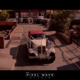 Pixel Wave Studio - Kremowy, zabytkowy samochód z czerwonym dachem, udekorowany białymi wstążkami, jedzie ulicą na tle grupy osób przed domem, prawdopodobnie podczas uroczystości ślubnej.