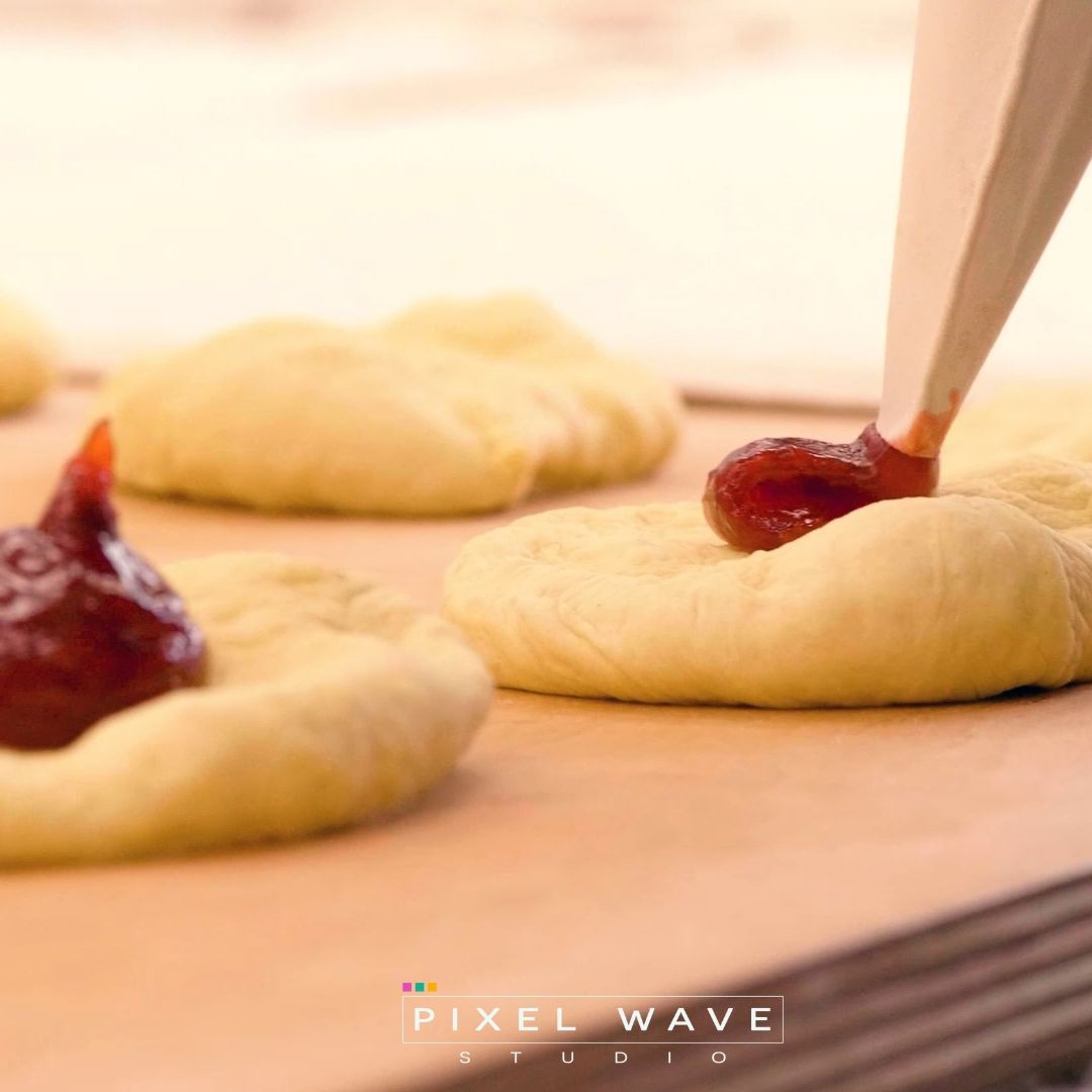 Nadziewanie surowych pączków marmoladą z rękawa cukierniczego na blasze do pieczenia.