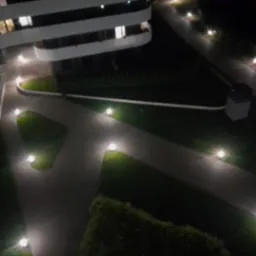 Nocny widok z góry na oświetloną ścieżkę w ogrodzie przy nowoczesnym budynku z balkonami, z wykorzystaniem niskich lamp ogrodowych.