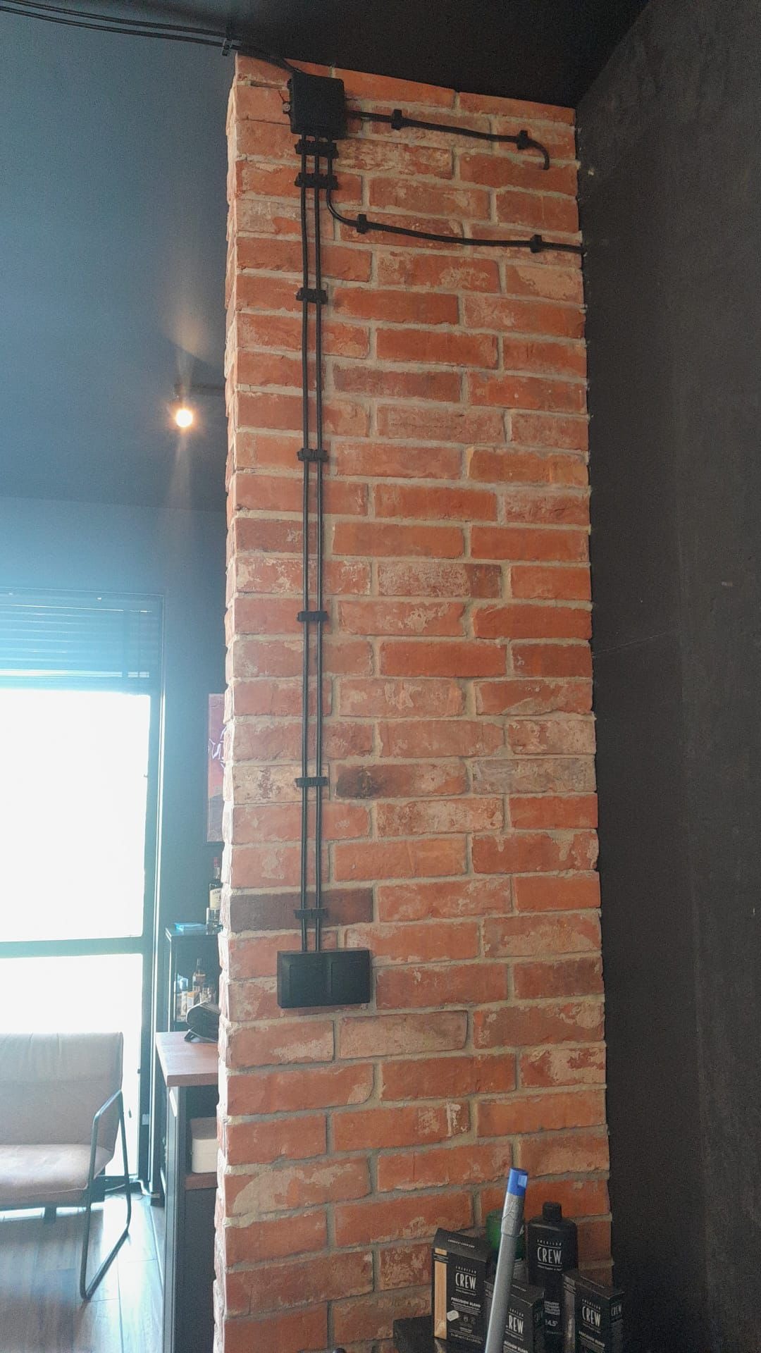 Czarne przewody elektryczne poprowadzone po ceglanej ścianie, widoczne uchwyty mocujące i puszka instalacyjna.