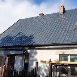 Roof Top - Pogotowie Dekarskie - Dom z nowym, grafitowym dachem z dachówki metalowej, widoczne kominy z cegły, okno dachowe i zamontowane rynny.