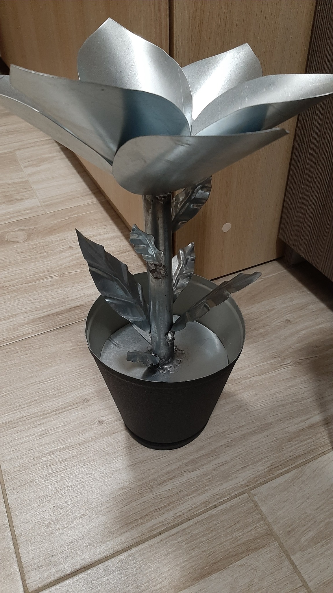 Dekoracyjna, ręcznie wykonana metalowa roślina z blachy w czarnej doniczce, spawana konstrukcja z widocznymi śladami obróbki.