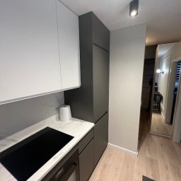 Igor Yarmolitskyi - Nowoczesna kuchnia w odcieniach bieli i szarości, z marmurowym blatem, płytą indukcyjną i widocznym fragmentem piekarnika. W tle widoczny fragment korytarza z lustrem.