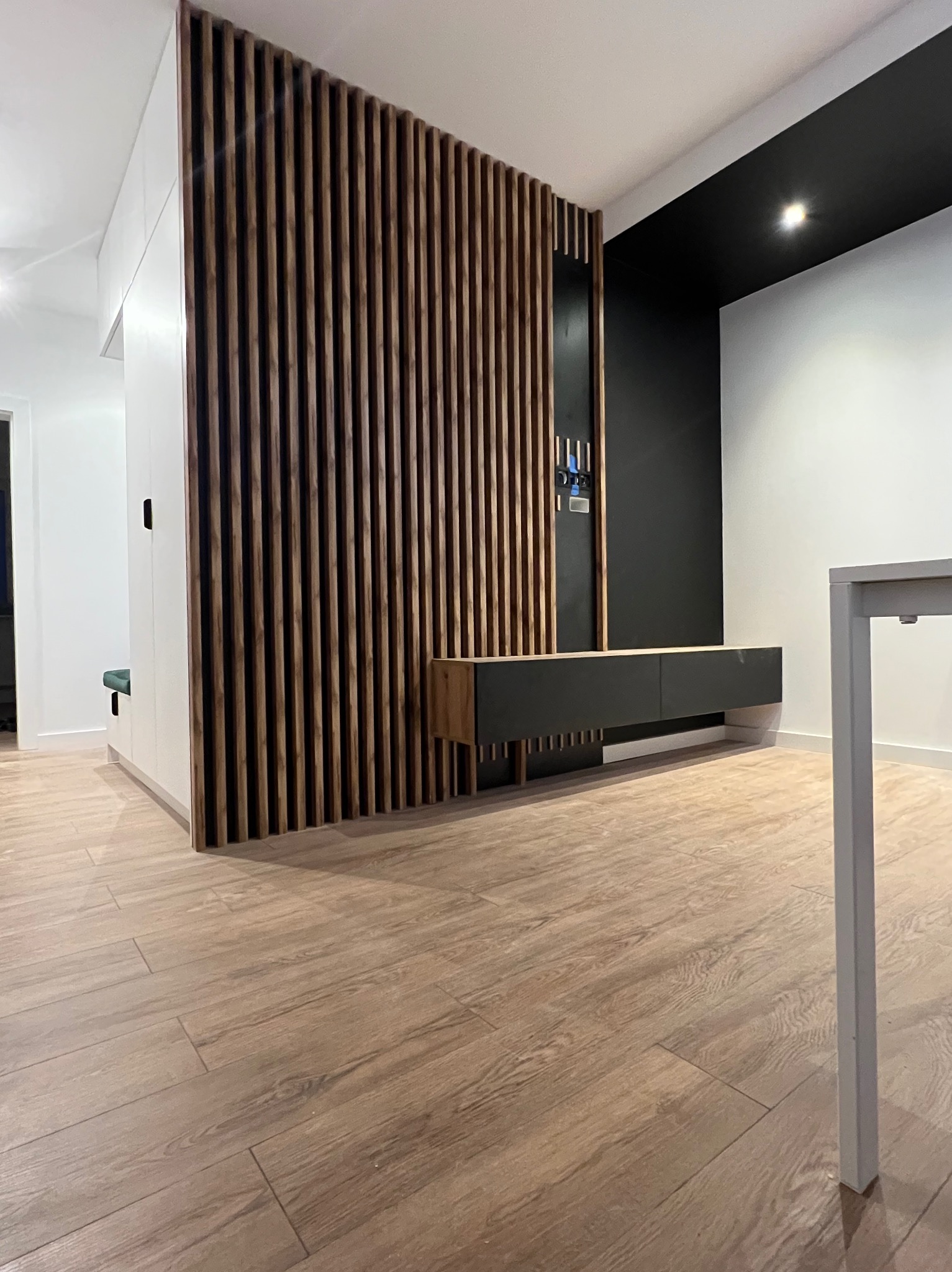 Nowoczesne wnętrze z drewnianą ścianką działową z lameli, szafką RTV w kolorze czarnym i podłogą imitującą drewno.