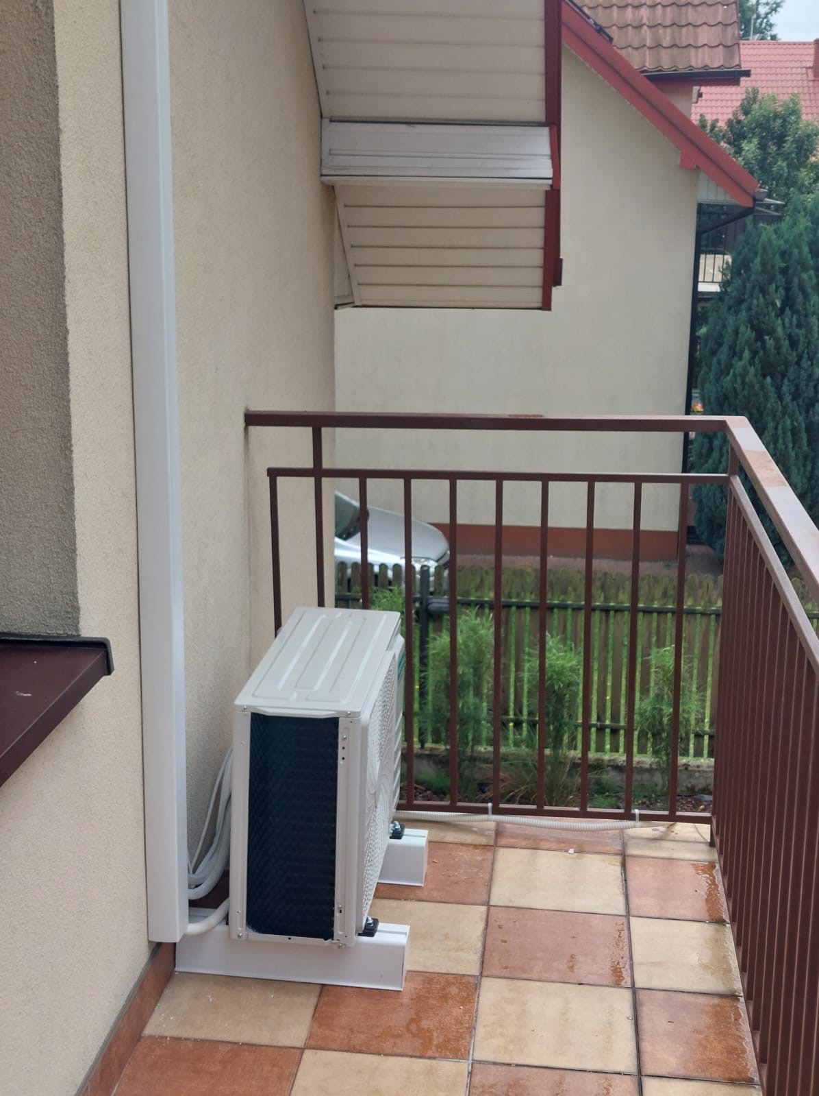 Zewnętrzna jednostka klimatyzacji zamontowana na balkonie domu jednorodzinnego, widoczne przewody i elementy montażowe.