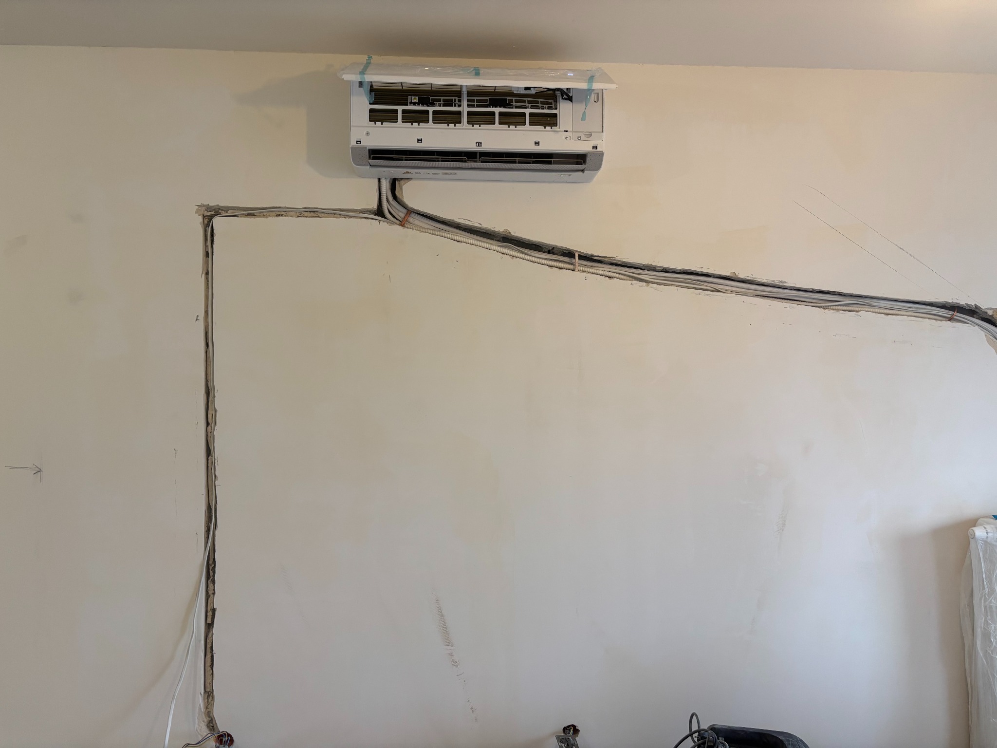 Montaż klimatyzacji na ścianie z wyciętymi bruzdami na przewody, widoczne kable i rury. Etap instalacji klimatyzacji w pomieszczeniu.