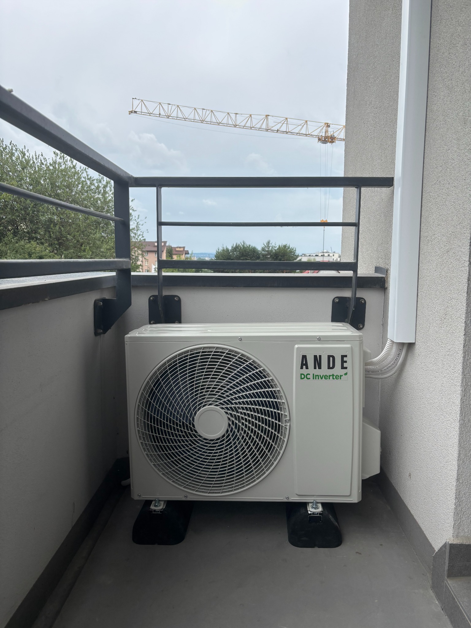 Jednostka zewnętrzna klimatyzacji ANDE DC Inverter zamontowana na balkonie, widok na budowę z dźwigiem w tle, instalacja w peszlu.
