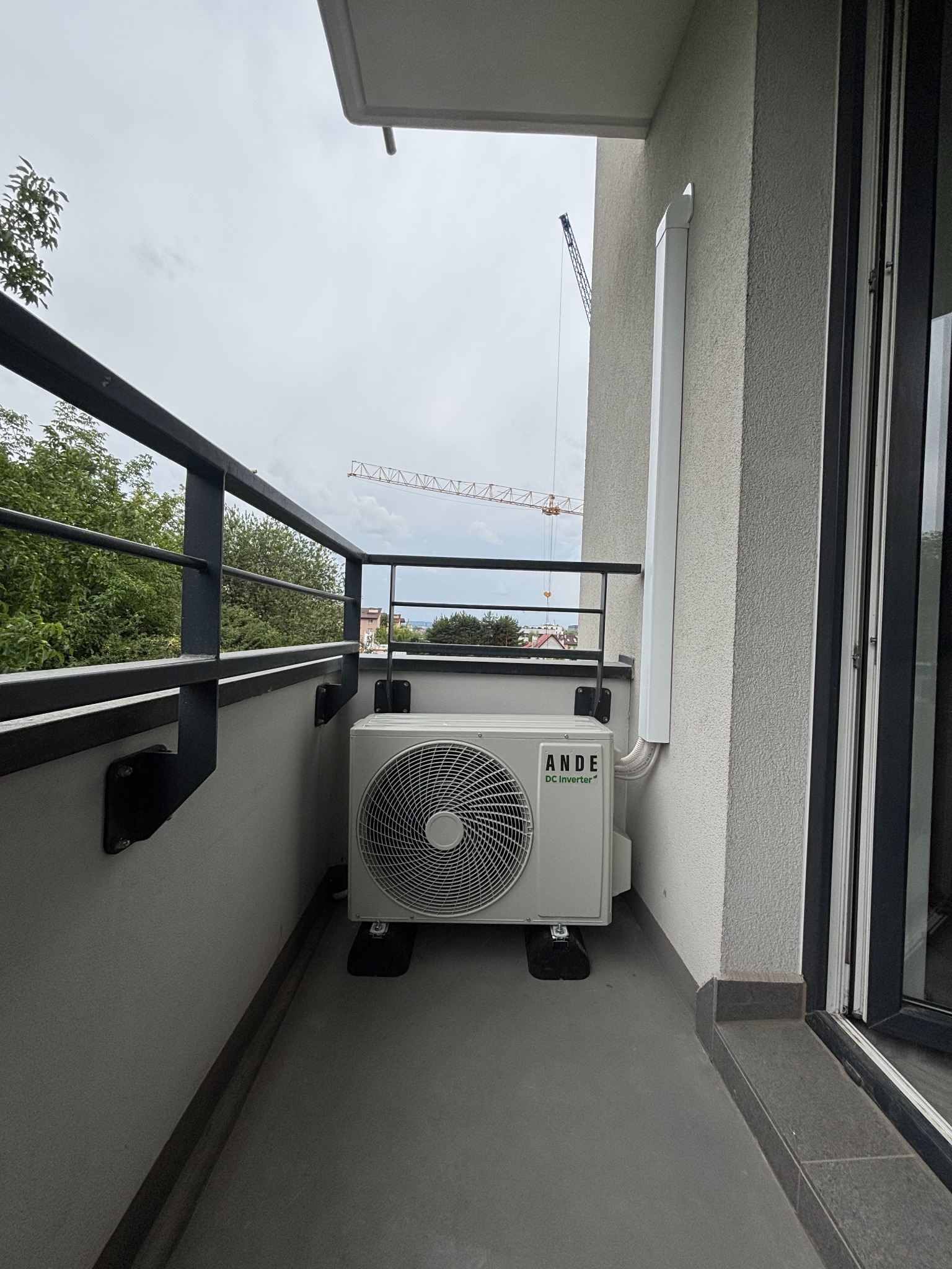 Zamontowana jednostka zewnętrzna klimatyzacji ANDE DC Inverter na balkonie z widokiem na budowę z dźwigiem. Estetyczny montaż instalacji.