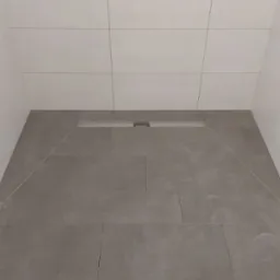 Nowoczesna kabina prysznicowa z szarymi płytkami podłogowymi i białymi płytkami ściennymi, widoczny odpływ liniowy i instalacja pod natrysk.