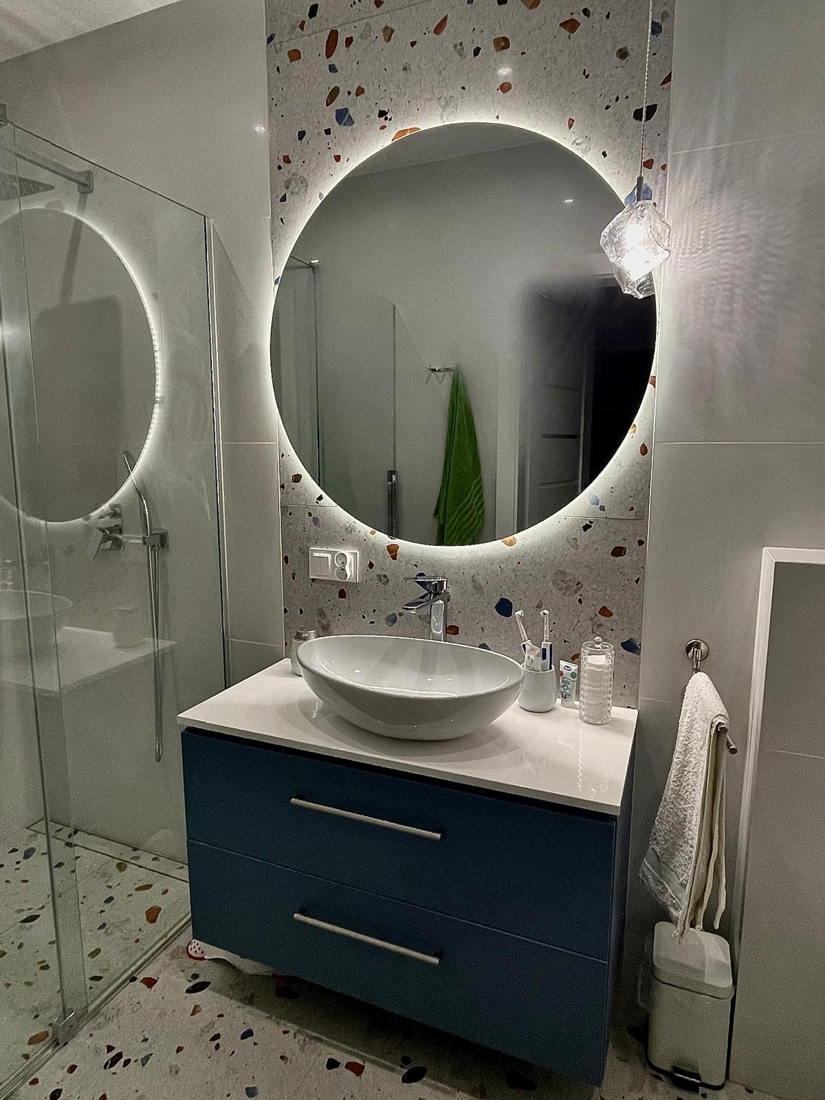 Nowoczesna łazienka z okrągłym lustrem LED, umywalką nablatową na szafce z szufladami w kolorze granatowym, płytki podłogowe i ścienne w stylu lastryko.