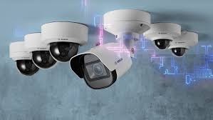 Zestaw kamer Bosch w różnych rozmiarach i kształtach, ustawionych na tle błękitnej, teksturowanej ściany. Widoczne efekty świetlne, sugerujące zaawansowaną technologię.